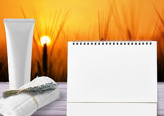 White cosmetic tube, towel, and calendar on wooden table with sunset background
