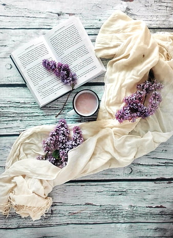 Flat lay of open book, lilac flowers, and coffee on rustic wood