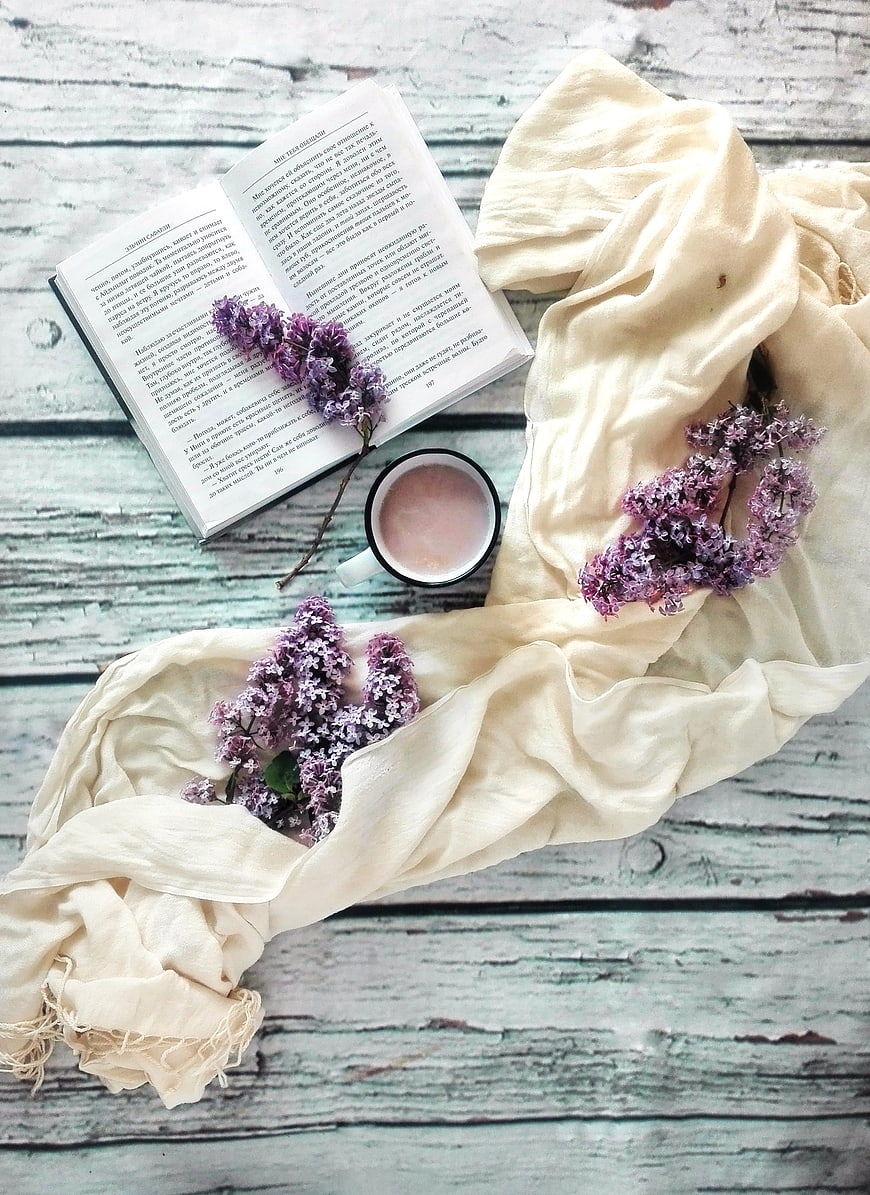 Flat lay of open book, lilac flowers, and coffee on rustic wood