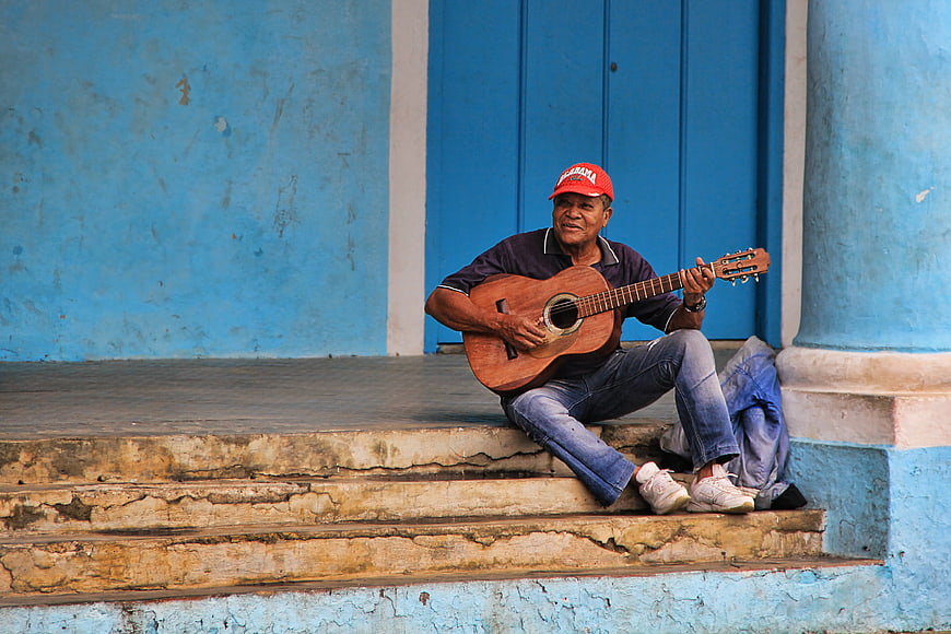 Senior Cuban Man Playing Acoustic Guitar On Blue Stairs