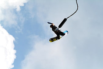 Snowboarder performing bungee jump against blue sky