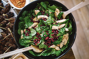 Top view of spinach chicken pomegranate salad with wooden spoons