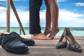 Barefoot couple on wooden deck with shoes and ocean view