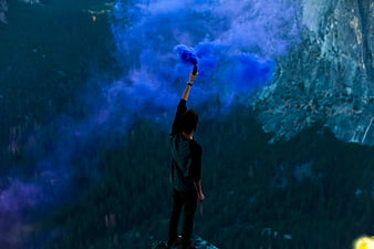 Man holding blue smoke flare on mountain peak