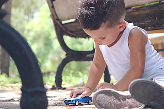 Toddler boy playing with blue toy car on ground