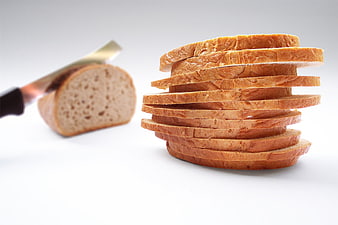 Stack of sliced bread with knife and loaf on white background