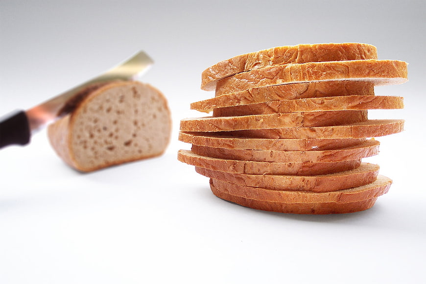 Stack of sliced bread with knife and loaf on white background