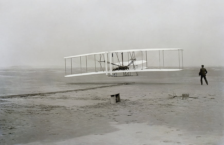 Historical Wright Brothers Flyer Aircraft Hovering Over Sand Dunes