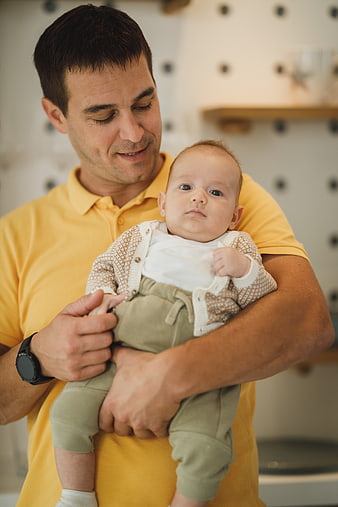 Father holding baby in yellow shirt at home