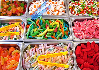 Assorted colorful gummy candies in metal bins with tongs