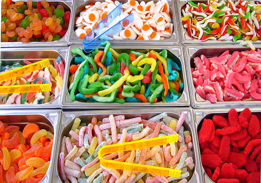 Assorted colorful gummy candies in metal bins with tongs