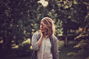 Thoughtful woman in striped shirt standing in park