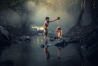 Two boys playing and splashing water in a misty forest river
