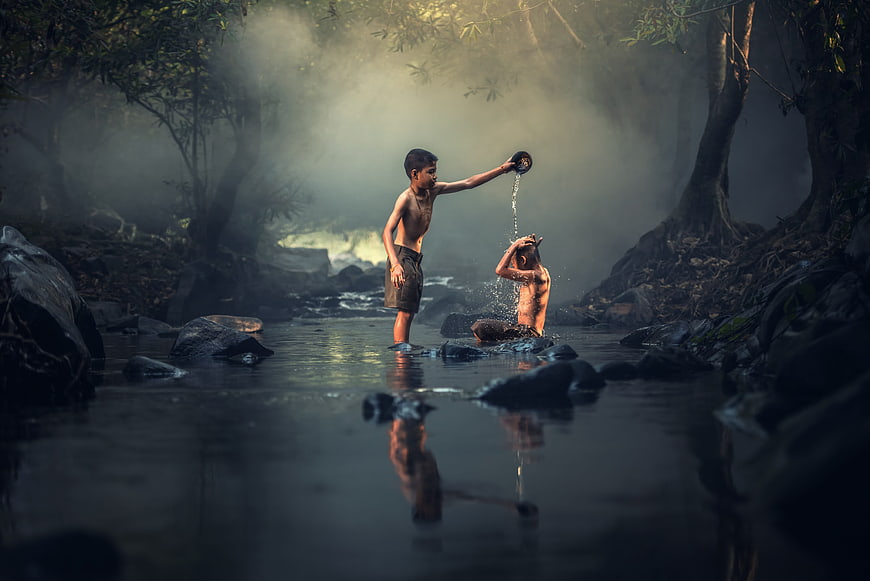 Two boys playing and splashing water in a misty forest river