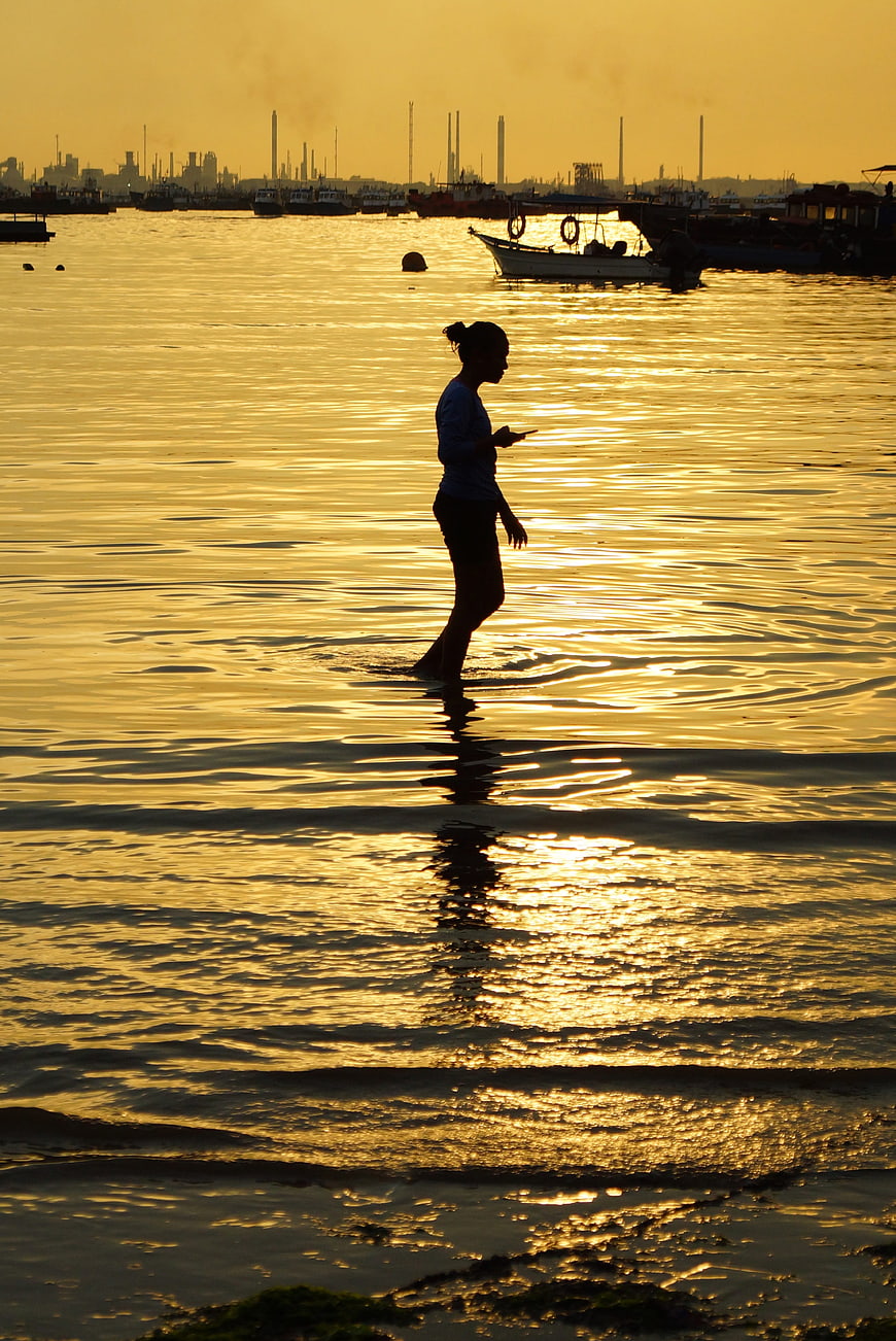 Silhouette of woman walking in shallow water at golden sunset