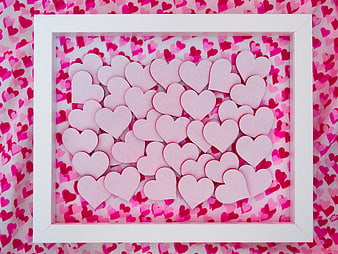 Pink paper hearts in white frame on patterned background