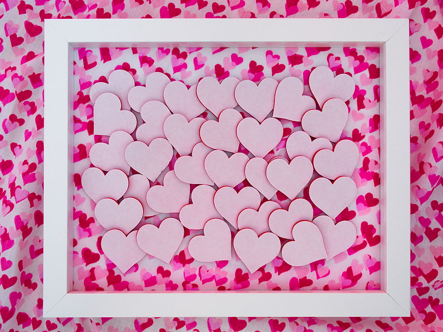 Pink paper hearts in white frame on patterned background