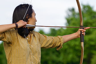 Woman drawing a traditional wooden bow and arrow outdoors