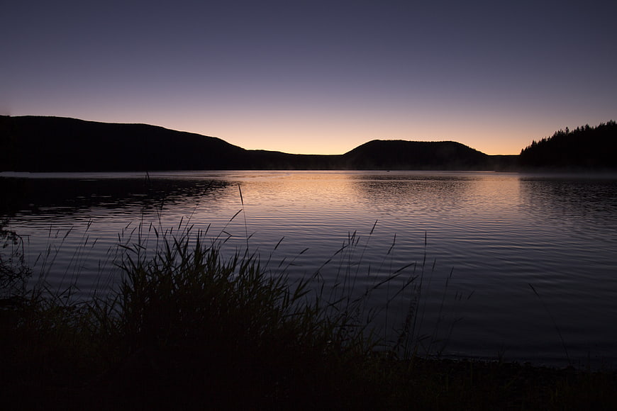 Serene Lake at Dusk with Silhouetted Hills and Reeds