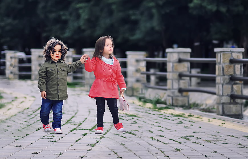Two young children walking together holding hands in a park
