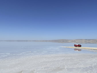 Red Van Parked on Salt Flat Shoreline Under Blue Sky