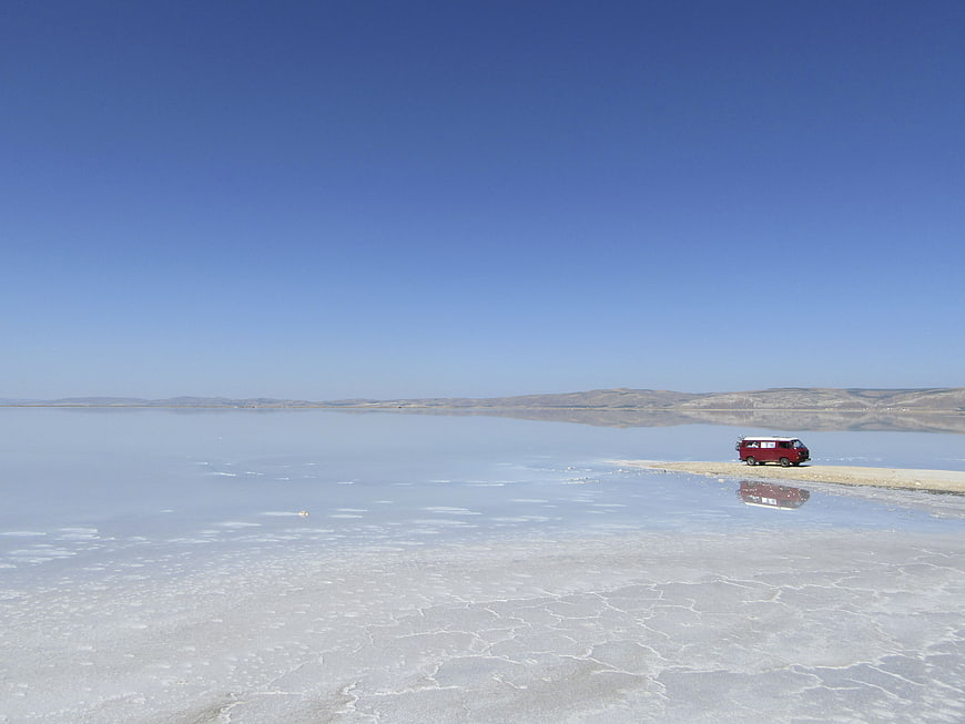 Red Van Parked on Salt Flat Shoreline Under Blue Sky