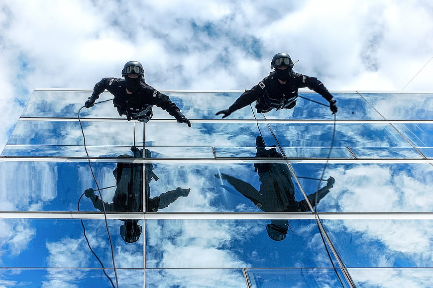 Two Window Cleaners on Glass Facade with Sky Reflection