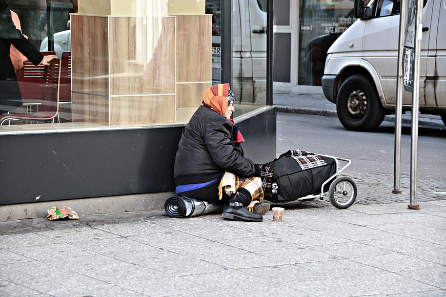 Homeless Woman Sitting On City Street With Cart