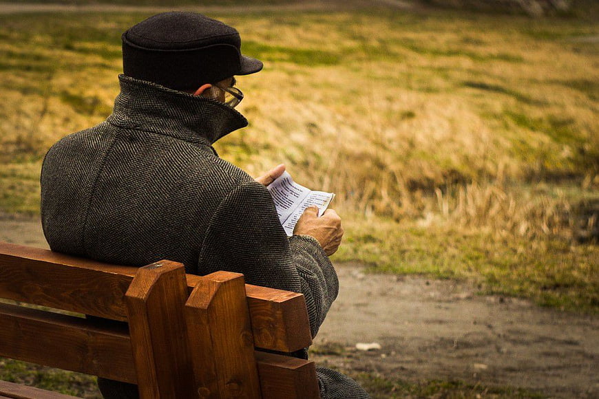 Senior Man Reading Book on Park Bench
