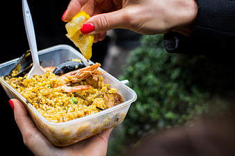 Hands squeezing lemon over seafood paella takeaway