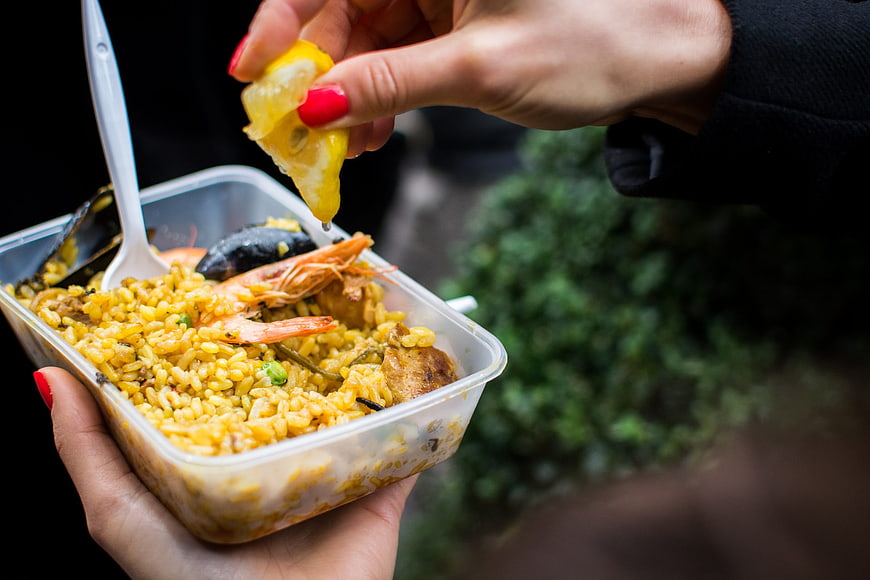 Hands squeezing lemon over seafood paella takeaway