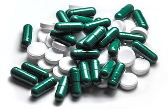Green capsules and white pills on white background