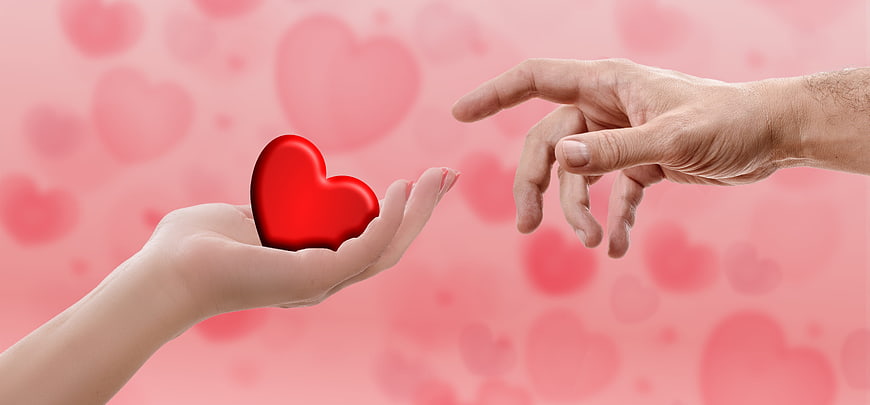 Hands exchanging red heart on pink background
