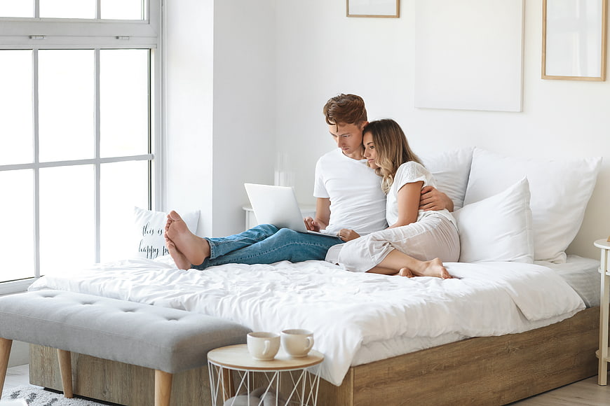 Young couple relaxing on bed using laptop in bright bedroom
