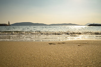 Low angle view of sandy beach with sparkling ocean waves and distant hills