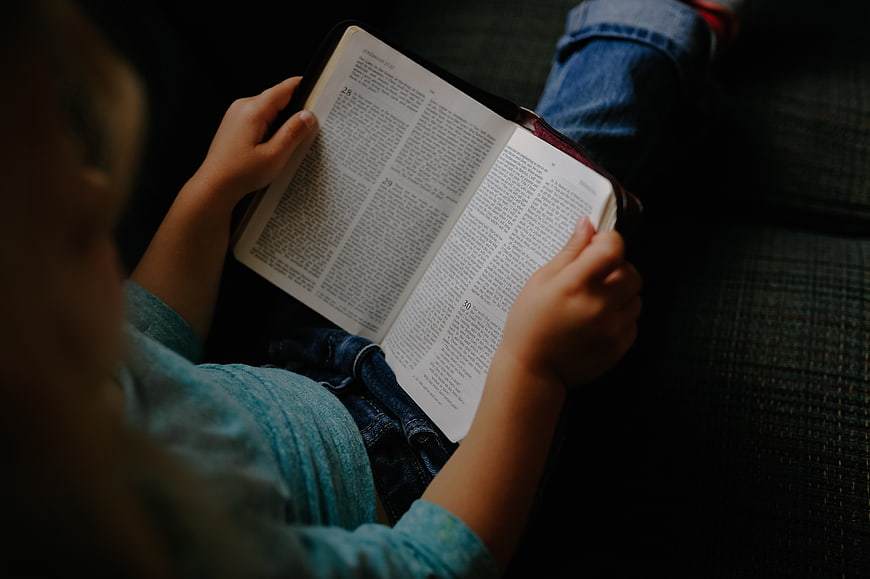 Child Reading Bible on Couch
