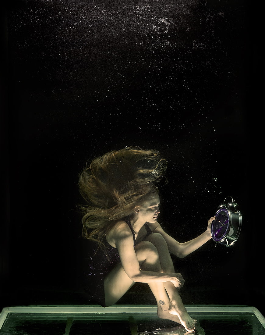 Underwater Portrait of Woman Holding Clock in Dark Water