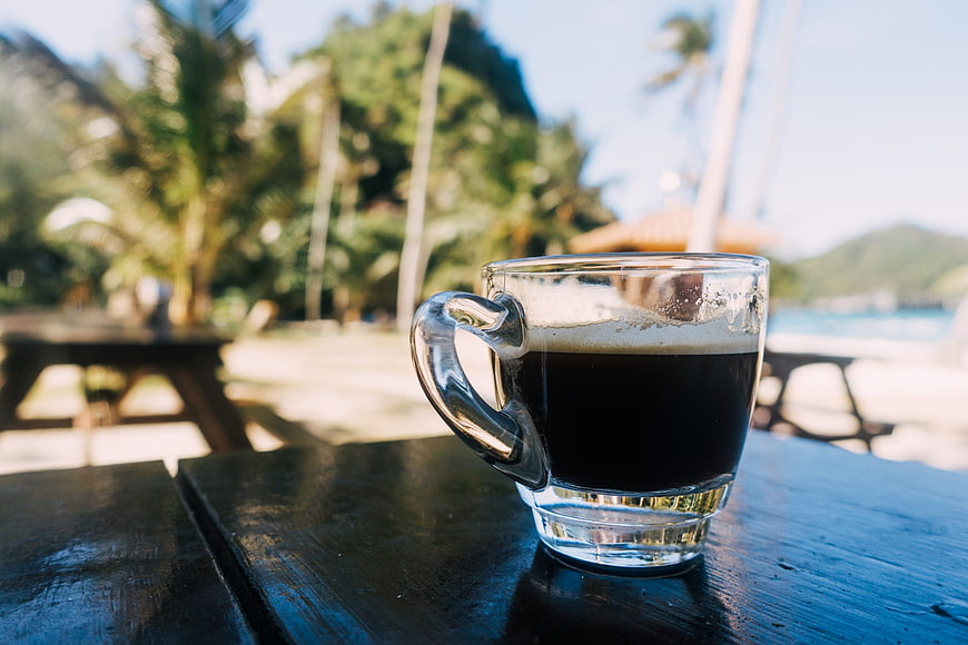 Glass of Black Coffee on Wooden Table by Tropical Beach