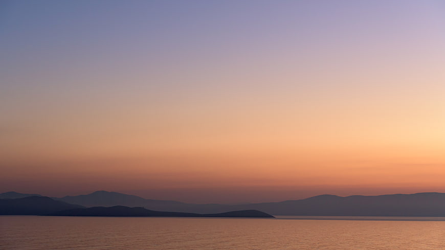 Serene Sunset Over Ocean with Mountain Silhouettes