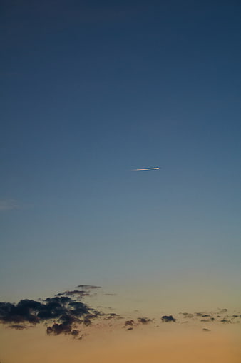 Airplane contrail streaking across twilight sky with clouds