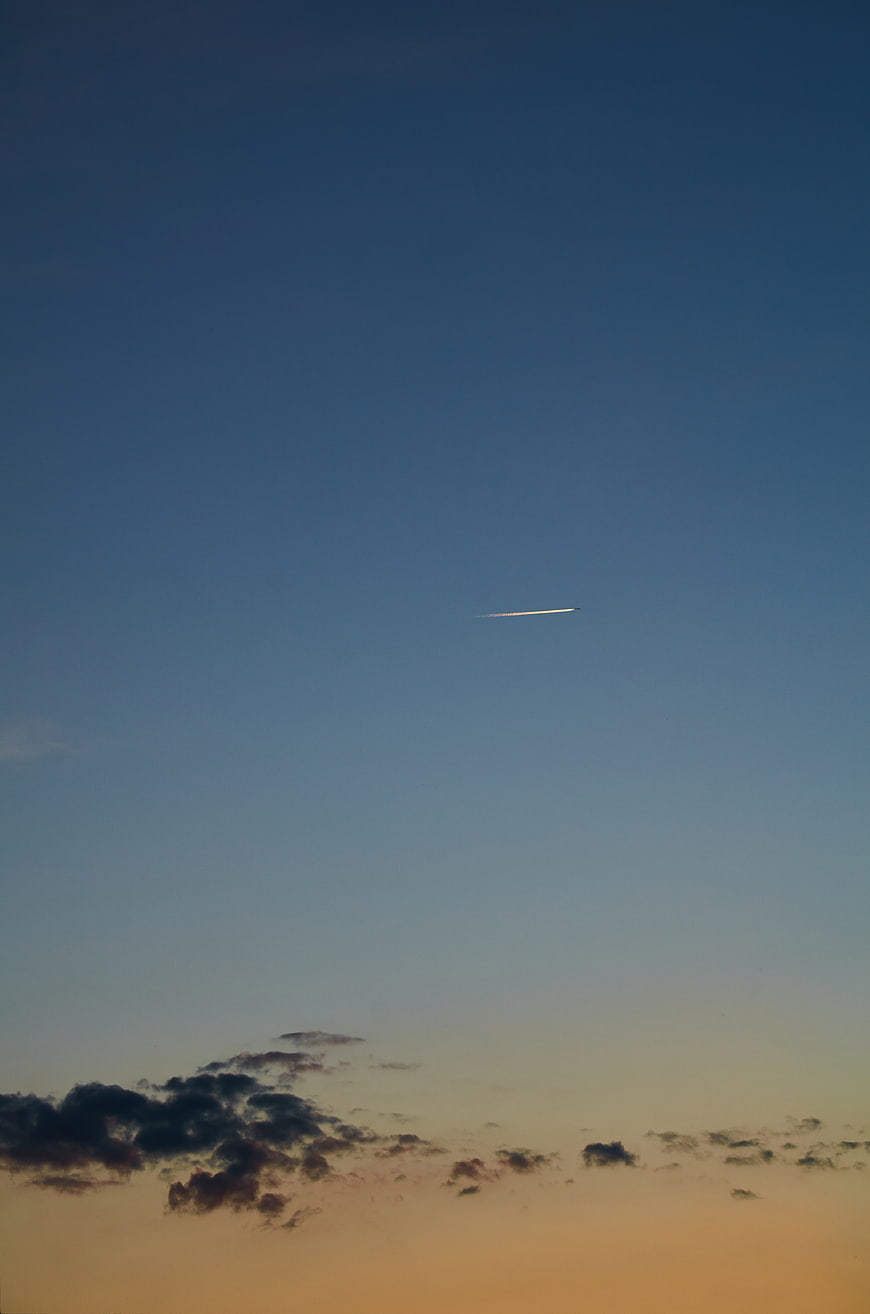 Airplane contrail streaking across twilight sky with clouds