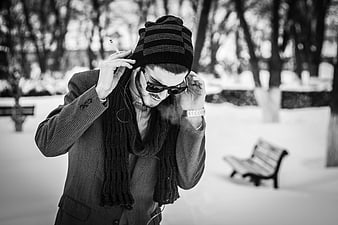 Man in winter coat smoking and listening to music in snowy park