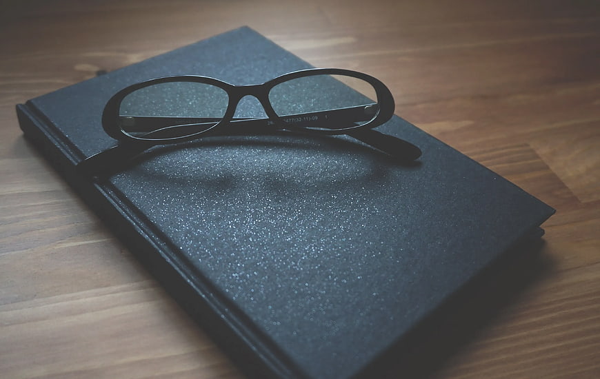 Black Eyeglasses on Textured Notebook on Wooden Table