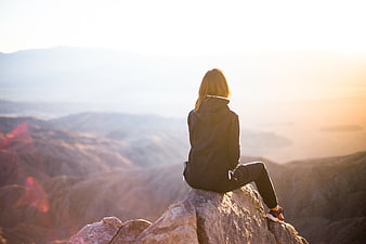 Woman sitting on mountain peak looking at sunset view