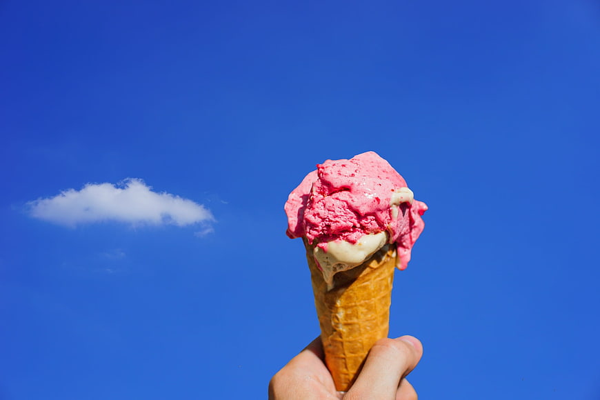 Hand holding pink ice cream cone against clear blue sky