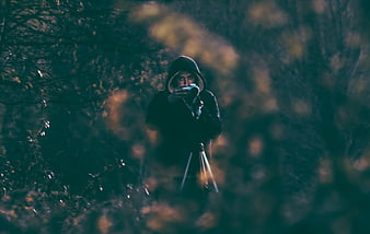Mysterious hooded photographer in dark forest with camera