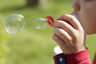 Child blowing soap bubbles outdoors in a sunny green park