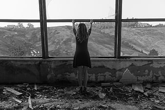 Woman standing in abandoned building looking out window at hills