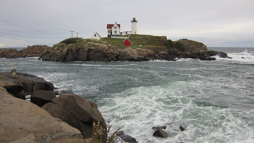 Coastal Lighthouse On Rocky Island With Churning Ocean Waves