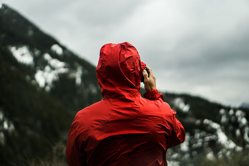 Person in red raincoat talking on phone in mountains